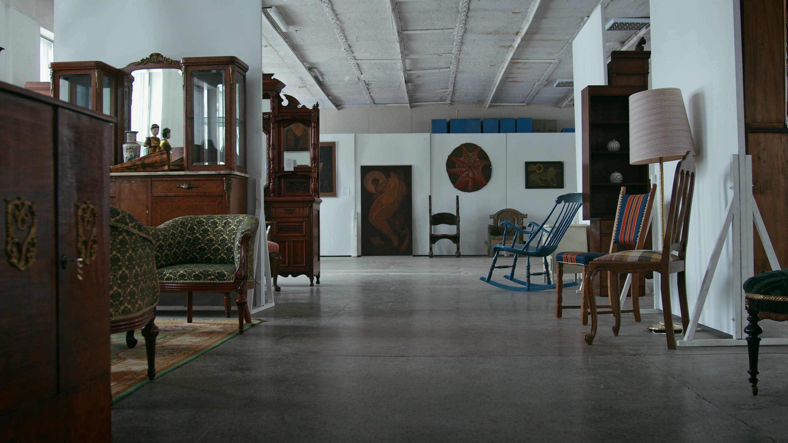 An antique showroom floor lined with carved wooden cabinets, upholstered chairs, and vintage lamps