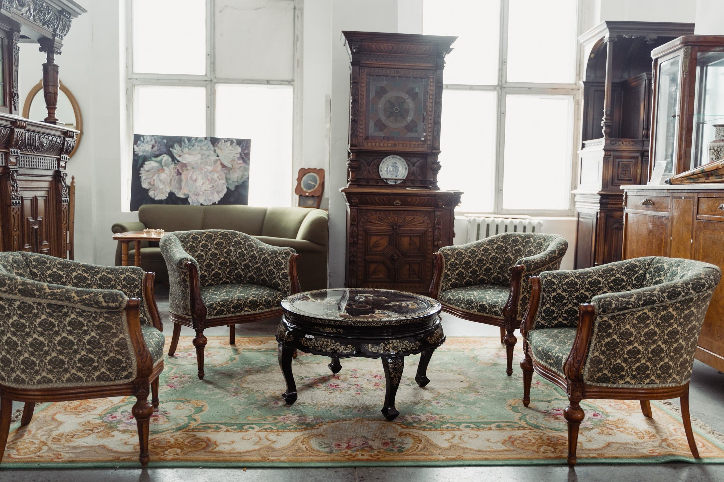 An ornate European antique parlor — damask armchairs around a lacquered coffee table, with a carved oak cabinet behind